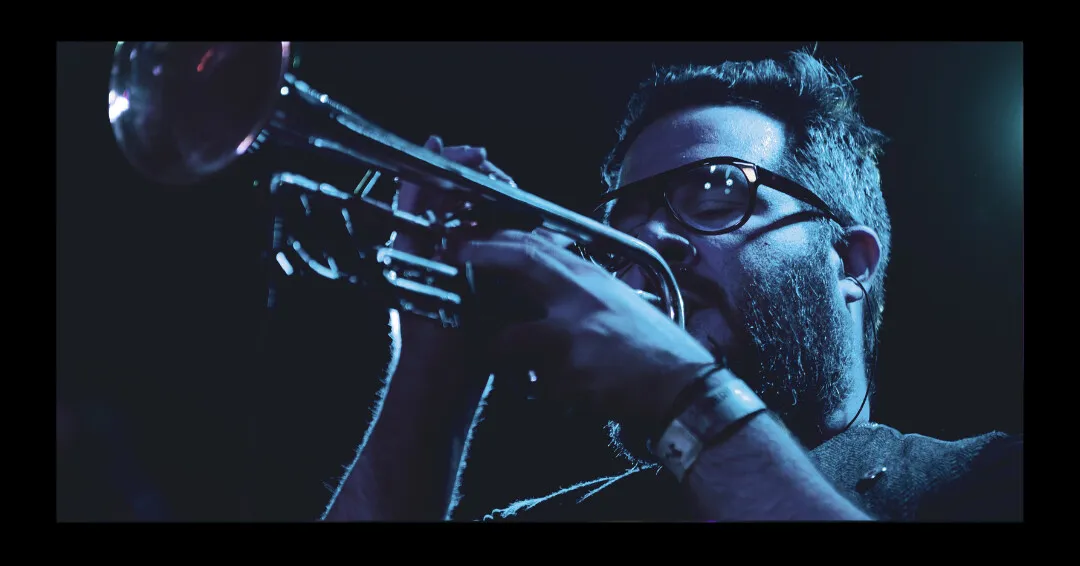 A Rock Star Brass trumpeter in close-up, playing under deep blue stage light.